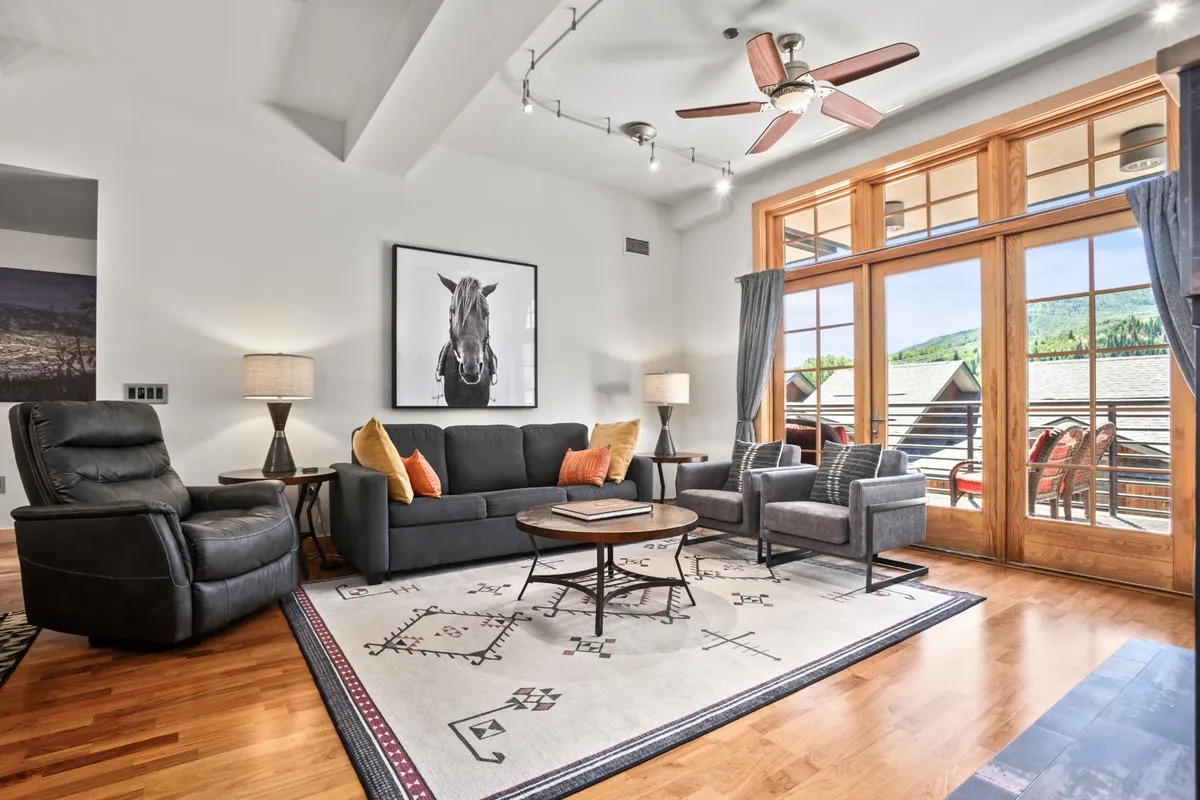 A cozy and upscale living area with large wooden-framed windows, an art piece of a horse, and a comfortable seating arrangement. The bright, airy space exudes a welcoming resort-like atmosphere, ideal for relaxing after adventure-filled days.