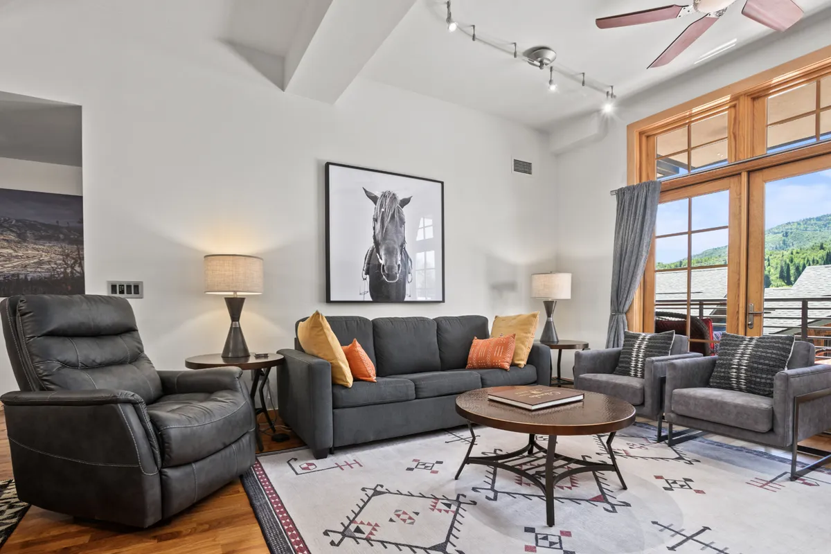 A cozy seating area featuring a large window overlooking a scenic view, with a coffee table and books in the foreground. The framed black and white horse photograph adds a touch of local charm and relaxation, while the expansive window hints at the inviting world just beyond.