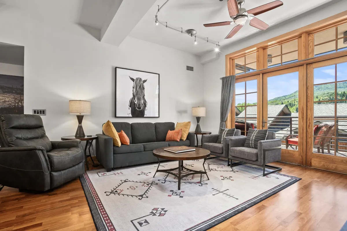 A bright and welcoming living space featuring a comfortable sofa, stylish armchairs, and large windows with a balcony view. The space is accented with a large horse portrait and is filled with natural light, inviting guests to relax while enjoying views that suggest proximity to local attractions.