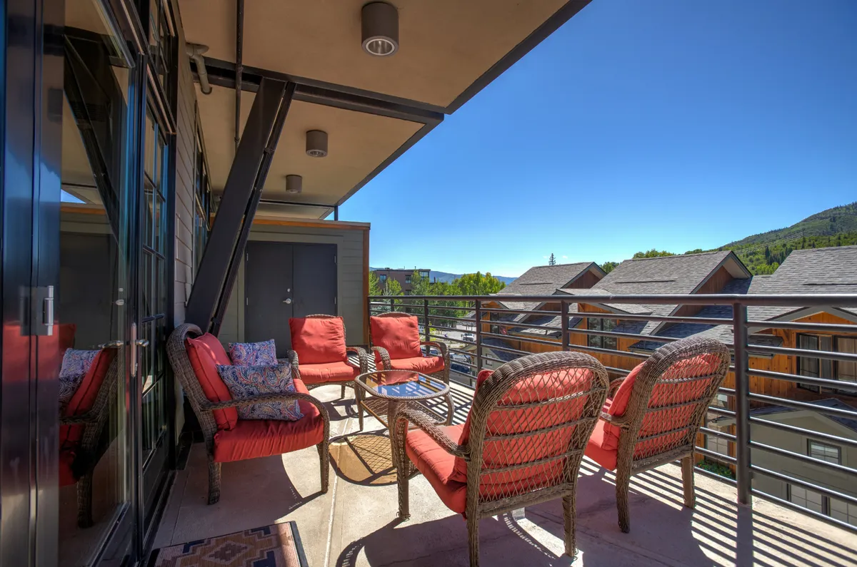 The hero image showcases the condo's inviting outdoor seating area with plush red cushioned chairs and a glass table, all set against a breathtaking backdrop of Steamboat Springs' mountain vistas. The space is ideal for relaxing, sipping morning coffee, or unwinding as the sun sets behind the peaks.