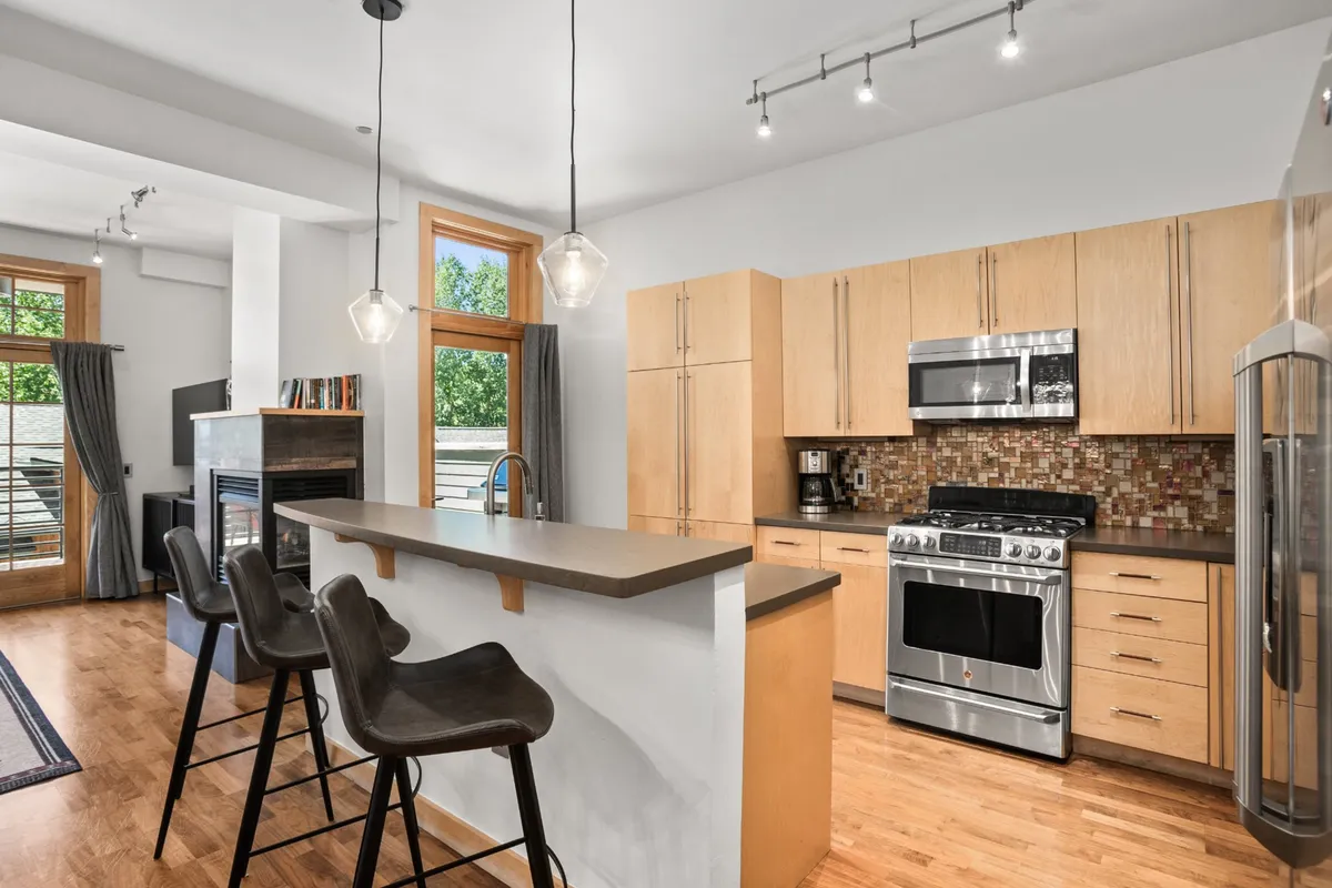 A kitchen and living area featuring a kitchen island, stainless steel appliances, large windows, and a fireplace. The open-plan space is ideal for gathering, sharing meals, and planning the next day’s adventure.