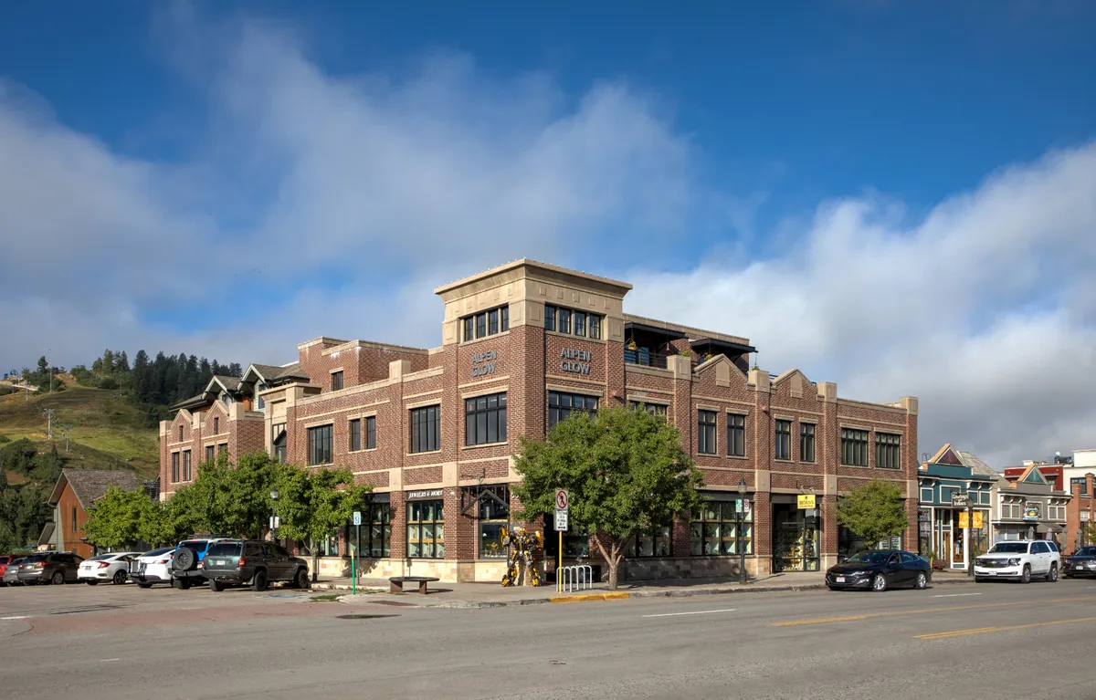 A lively downtown street scene featuring a classic brick façade, large windows, tree-lined sidewalks, and visible street signage. The environment is bustling yet welcoming, with people walking and abundant natural light accentuating the vibrancy. The setting suggests close proximity to shopping, dining, and entertainment options.