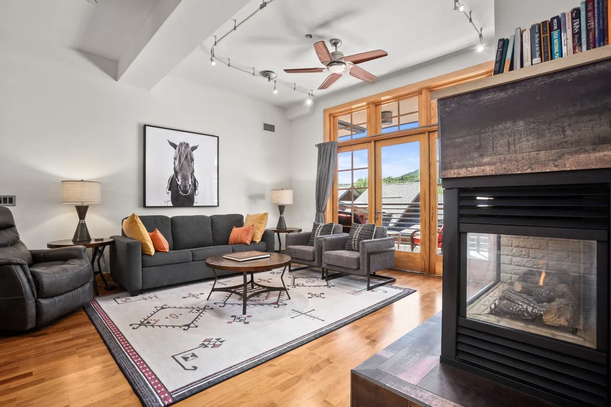 A stylish living room with a sofa adorned with orange cushions, distinctive horse artwork, a fireplace, and expansive windows filling the space with light. The layout is perfect for relaxing or socializing before or after a day of exploring the local area.