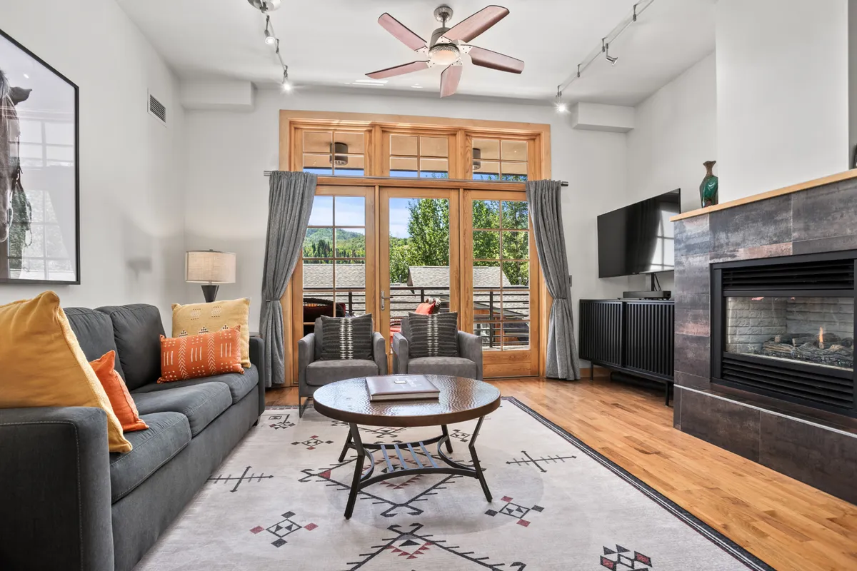 A cozy living area featuring large windows that offer scenic views of the surrounding area, a fireplace, comfortable seating with decorative pillows, and a coffee table. Abundant natural light pours in, visually connecting the indoors to the outdoors and inviting relaxation after an active day.