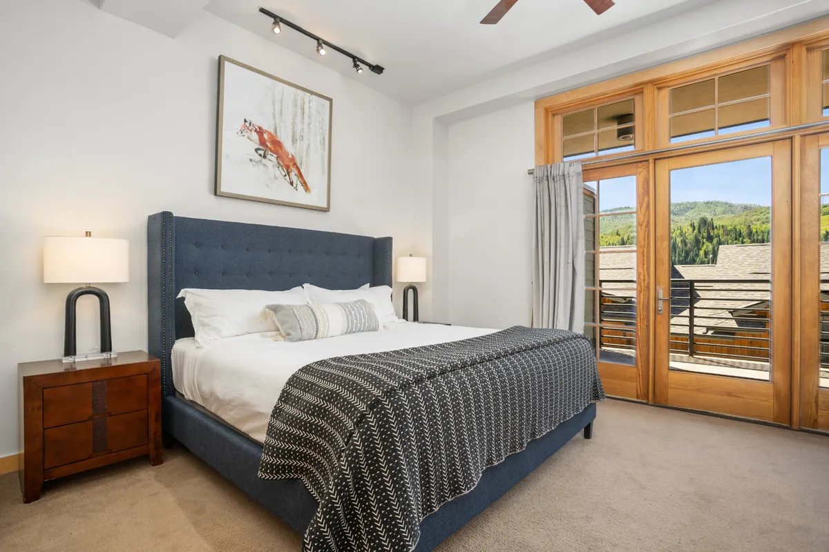 A calm, serene bedroom featuring a large king bed as the focal point. Double doors open to a scenic outdoor view, and the room is accented with tasteful wall art. Soft linens and a tranquil atmosphere invite relaxation and restful sleep.